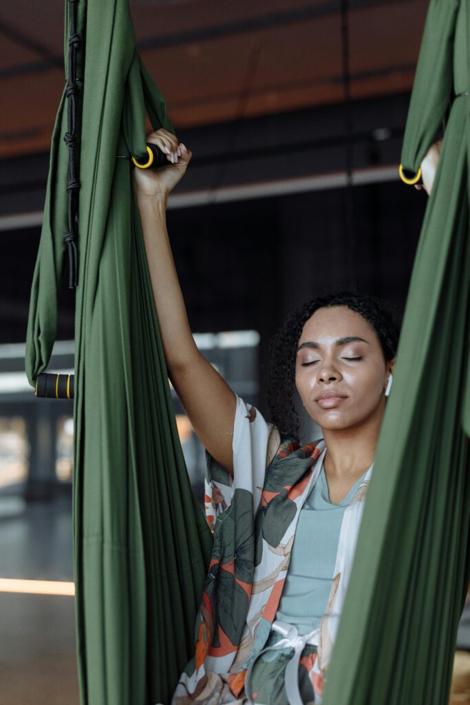 Serene young woman meditating in a green hammock indoors, eyes closed, enjoying tranquility.