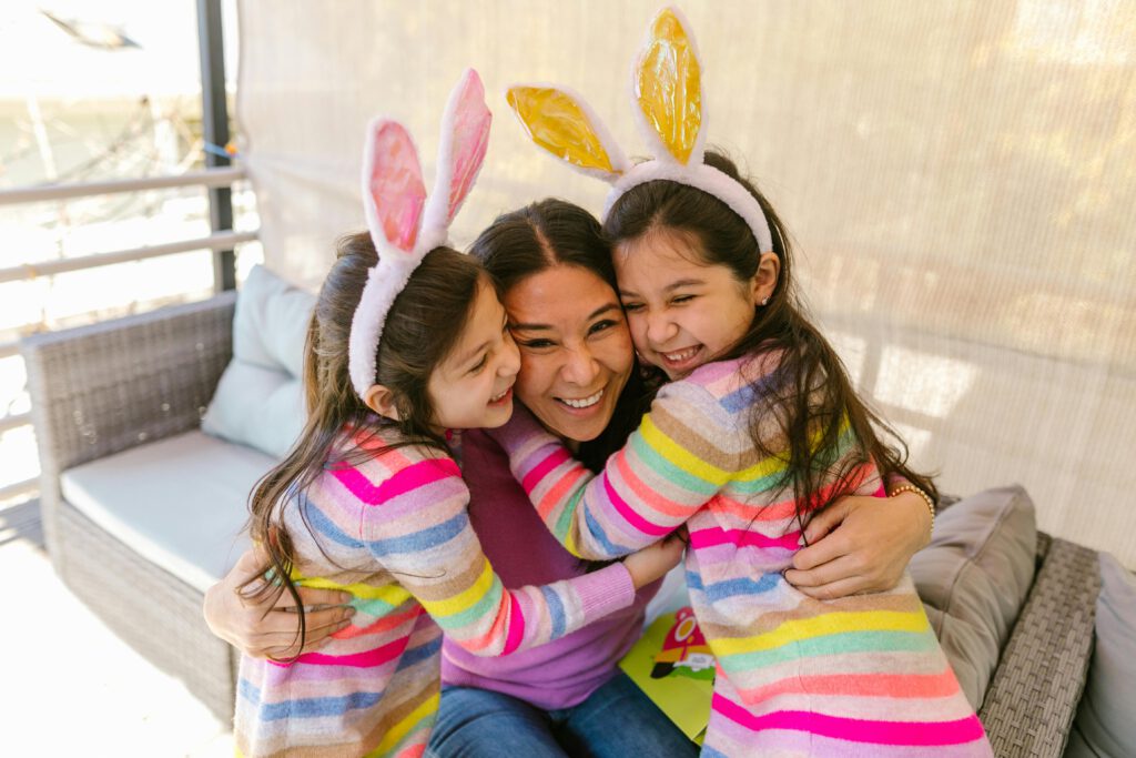 A joyful mother and her daughters, wearing bunny ears, share a warm embrace indoors. Perfect for family and holiday themes.